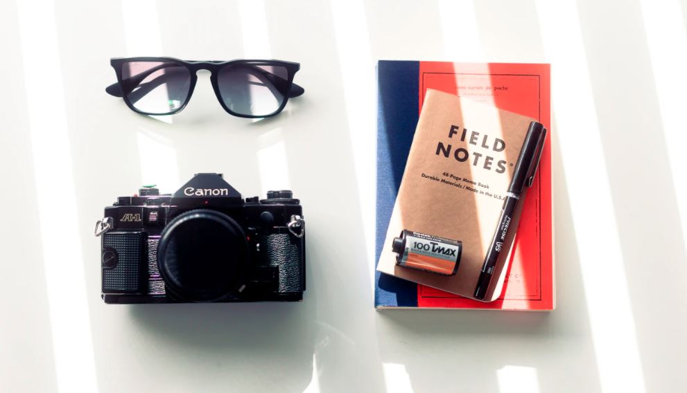 Flat lay image of a camera, book and sunglasses.